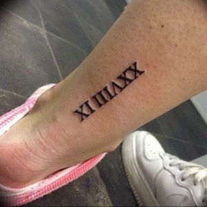 Черно-белое фото татуировки на лодыжке с римскими цифрами XIX IIIIX. Простой и лаконичный дизайн, четкие линии, изящный рисунок.