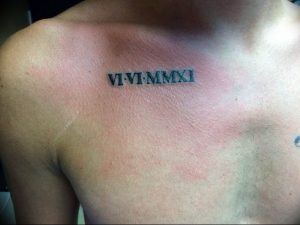 Черно-белое фото татуировки на груди с римскими цифрами VI-VI-MMXI. Простой и лаконичный дизайн, четкие линии, символ важной даты.