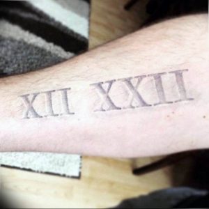 Черно-серое фото татуировки на предплечье с римскими цифрами XII XXII. Минималистичный дизайн, четкие линии, простой и элегантный рисунок.
