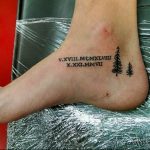 Фото татуировки на лодыжке с изображением римских цифр 'V.XVIII.MCMXLVIII X.XXI.MMVII' и двух небольших елей.