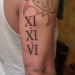 Фото тату: римские цифры 'XI XI VI' на бицепсе мужчины, выполненные в стиле олд скул. Черный цвет, толстые линии, яркие элементы.