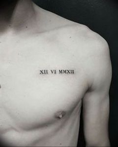Фото тату: черные римские цифры 'XII VI MMXXII' на груди молодого человека. Минималистичный дизайн, четкие линии, небольшое изображение.