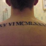 Фото тату на спине, в области шеи и лопаток, с черными римскими цифрами XXV VI MCMLXXXIX. Изогнутая линия, минималистичный дизайн.