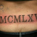 Фото тату на пояснице с черными римскими цифрами MCMXLXV, обозначающими год 1945. Классический шрифт, четкие линии, минималистичный дизайн.