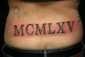 Фото тату на пояснице с черными римскими цифрами MCMXLXV, обозначающими год 1945. Классический шрифт, четкие линии, минималистичный дизайн.