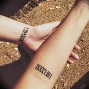 Фото парных тату с римскими цифрами I.XIII.II-I и III.XXIII.I на запястьях. Черный цвет, минималистичный дизайн, символизирующий связь между двумя людьми.