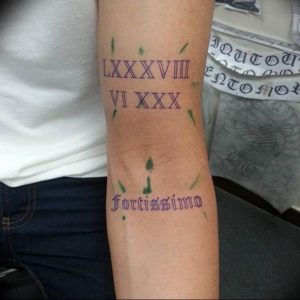 Фото тату с римскими цифрами LXXXVVIII VI XXX и латинской фразой 'Fortissimo' на руке. Черный цвет, стильный дизайн, вдохновляющее значение.