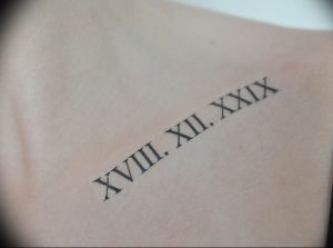 Фото тату с черными римскими цифрами XVIII.XII.XXXIX на лопатке. Минималистичный дизайн, четкие линии, аккуратное исполнение.