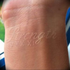 Фотография белой татуировки на запястье с надписью "Strength" и римскими цифрами "IV XX XI", выполненной тонкой линией.