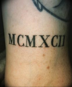 Фотография татуировки на руке с римскими цифрами "MCMXCII", символизирующими год 1992.