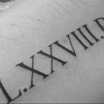 Фотография простой татуировки с римскими цифрами "LXXVIII.R" на коже, выполненной в черном цвете.
