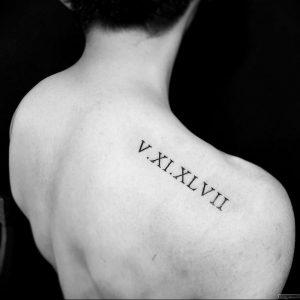 Фото тату: черные римские цифры 'V.XI.XLVII' на плече. Минималистичный дизайн, четкие линии, подчеркивает изящество и женственность.