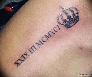 Фото тату: черные римские цифры 'XXIX.III.MCMXCI' и небольшая корона на плече. Символизирует власть, величие и значимую дату.