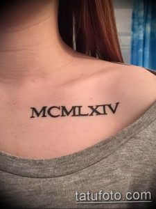 Фото тату: черные римские цифры 'MCMLXIV' на плече девушки. Изящный дизайн, четкие линии, подчеркивает женственность.