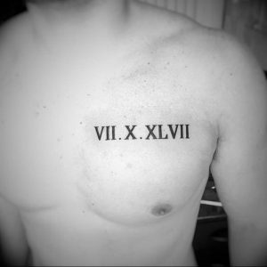 Фото тату: черные римские цифры 'VII.X.XLVII' на груди мужчины. Минималистичный дизайн, четкие линии, акцент на мужественности.