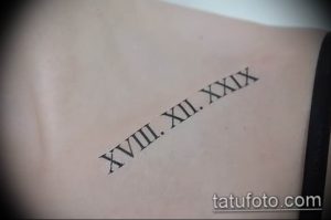 Фото тату на спине с римскими цифрами 'XVIII. XII. XXIX', выполненной черными чернилами. Изящный и минималистичный дизайн.