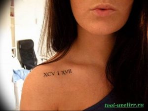 Фото тату: На ключице женщины изображена татуировка в виде римских цифр XCV I XVII. Элегантный и минималистичный дизайн.