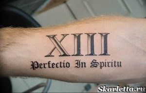 Фото тату: На руке изображена татуировка в виде римских цифр XIII и латинской фразы "Perfectio In Spiritu". Стильный и значимый дизайн.