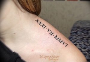 Фото тату с римскими цифрами XXXI.VII.MMVI на плече девушки. Черный рисунок татуировки выполнен аккуратным шрифтом.