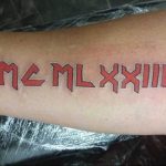 Фото тату с красными римскими цифрами MCMLXXIIII на руке. Яркий рисунок татуировки выполнен смелым шрифтом, привлекает внимание.