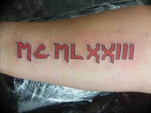 Фото тату с красными римскими цифрами MCMLXXIIII на руке. Яркий рисунок татуировки выполнен смелым шрифтом, привлекает внимание.