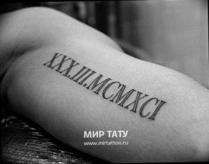 Фото тату с римскими цифрами XXX.III.MCMXCI на руке. Черный рисунок татуировки выполнен аккуратным шрифтом, выглядит стильно и минималистично.