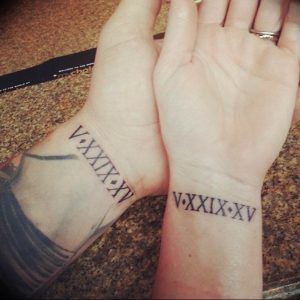 Фото парных татуировок на запястьях с римскими цифрами 'V.XXIX.XV'. Минималистичный дизайн для любящих пар.