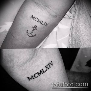Фото тату: черная татуировка с изображением якоря и римских цифр 'MCMXLIX' на запястье. Морская тематика и минималистичный дизайн.