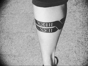 Фото тату: римские цифры XXIII и XXII на ноге, выполненные в виде браслета. Черный рисунок татуировки.