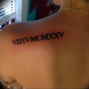 Фото тату: Простая татуировка с римскими цифрами VIII IV MCM XXV на плече. Черный цвет, тонкие линии, лаконичный дизайн.