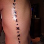 Фото тату: длинная вертикальная татуировка с римскими цифрами 'I V XIV I MCMCLXXII' на боку человека.