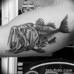 Фото тату: реалистичный рисунок скелета рыбы с детально прорисованной головой, выполненный на руке в черно-серых тонах.