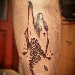 Фотография татуировки на ноге, изображающей руку, держащую скелет рыбы, с добавлением элементов в стиле олдскул.