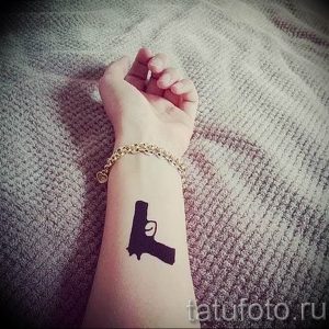 Фото тату небольшого черного пистолета на запястье девушки. Минималистичный и стильный рисунок.