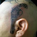 Фото тату: маленькая, минималистичная татуировка пистолета на голове. Смелый и необычный выбор для тех, кто хочет выделиться.