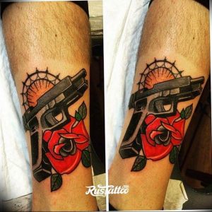 Фото тату пистолета и красной розы на предплечье. Черно-серый рисунок татуировки с яркими красными акцентами. Идея для тату для мужчин и женщин.