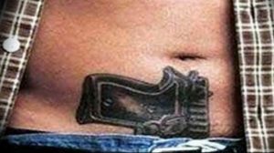 Фото тату простого эскиза пистолета на мужском животе. Черно-белый рисунок с минимальной детализацией.