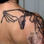 Фото татуировки на спине с изображением скелета ворона, летящего на фоне темного фона. Черно-белые тона, графический стиль, детализированная проработка, подходит для любителей готики.