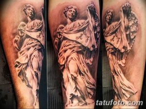 Черно-серая татуировка на ноге, изображающая античную статую женщины в одеянии, с детально проработанными складками ткани и украшениями, выполненная в реалистичном стиле.