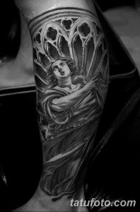 Фото татуировки на ноге с изображением ангела, окруженного готическими арками. Черно-белая гамма, детализированная проработка.