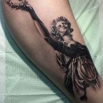 Фото татуировки на руке: изображение греческой богини Ники с лавровым венком, выполненное в черно-серых тонах с плавными линиями и детальной проработкой.