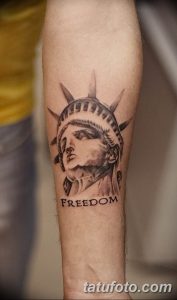 Фото тату с изображением головы Статуи Свободы и надписью "FREEDOM" на предплечье. Выполнено в черно-серых тонах, в минималистичном стиле.