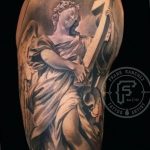 Черно-белое фото татуировки на руке с изображением ангела. Реалистичный стиль, детализированный рисунок, мягкие тени.