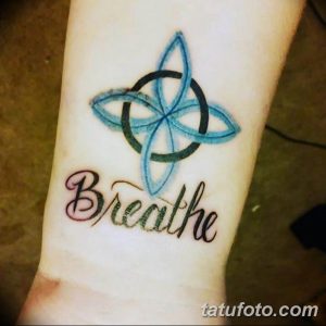Фото тату кельтского узора в форме клевера и надписи "Breathe" на руке. Цветная татуировка с голубыми и розовыми элементами.