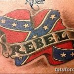 Фото тату конфедеративного флага с надписью 'Rebel'. Красные, белые и синие цвета, лента с надписью, смелый и противоречивый дизайн.