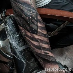 Фото тату на всю руку, изображающее американский флаг в черно-серых тонах, выполненное в стиле реализм с добавлением узора.