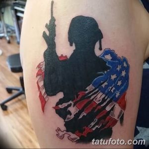 Фото тату с изображением солдата в форме и американского флага, символизирующего патриотизм, честь и защиту родины.