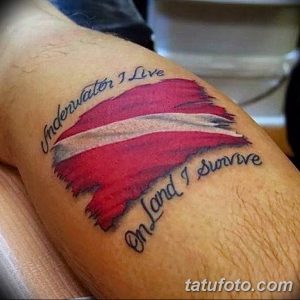Фото тату флага Латвии на руке с надписью 'Underwater I Live On Land I Survive'. Рисунок татуировки в красных и белых тонах.