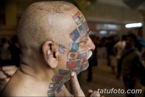 Фото тату: пожилой мужчина с татуировками флагов разных стран на лице и теле, выполненные в ярких цветах.