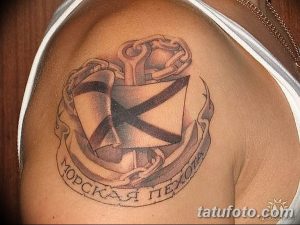 Фото тату на плече: изображение якоря, обвитого лентой с надписью "Морская пехота". Черно-белая татуировка, выполненная в классическом стиле.